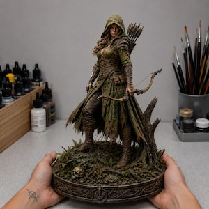 Könnte beinhalten: Eine detaillierte Fantasy-Figur eines Bogenschützen mit grünem Kapuzenumhang, brauner Lederrüstung und Stiefeln. Die Figur hält einen Holzbogen, trägt einen Köcher mit Pfeilen auf dem Rücken und steht auf einem moosigen Sockel mit einem kleinen Totenkopf.