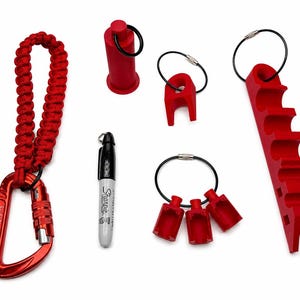 May include: A collection of red plastic tools including a carabiner with a braided red cord lanyard, a black Sharpie marker, a cylindrical cap, a single-slot holder, a three-slot holder, and a long multi-slot rack, all featuring black metal rings.