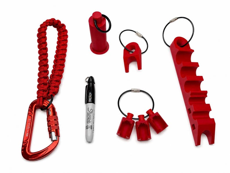 May include: A collection of red plastic tools including a carabiner with a braided red cord lanyard, a black Sharpie marker, a cylindrical cap, a single-slot holder, a three-slot holder, and a long multi-slot rack, all featuring black metal rings.