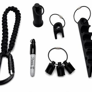 May include: A collection of black tactical gear including a carabiner with a braided paracord lanyard, a Sharpie marker, a cylindrical tool, a single-slot holder, a three-slot holder, and a long multi-slot organizer, all featuring metal rings.