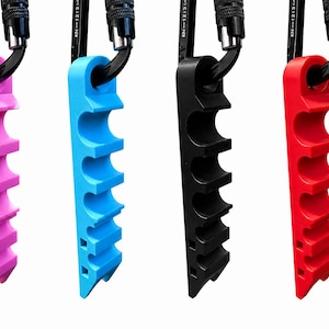 May include: Four climbing holds in pink, blue, black, and red are attached to black carabiners. Each hold has five rounded finger slots. The holds are made of a solid material and are designed for rock climbing or bouldering.