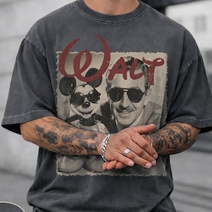 Puede incluir: Camiseta gris oscuro con un gr&aacute;fico vintage de Mickey Mouse con gafas de sol y Walt Disney. La palabra "Walt" est&aacute; en escritura roja encima de la imagen. La camiseta tiene un cuello redondo cl&aacute;sico.