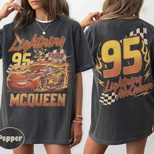 Puede incluir: Camiseta gris oscuro con un dise&ntilde;o de Rayo McQueen de la pel&iacute;cula Cars. El dise&ntilde;o frontal incluye el n&uacute;mero 95, el nombre del personaje y llamas. La parte trasera de la camiseta tambi&eacute;n muestra el n&uacute;mero 95 y el nombre de Rayo McQueen.
