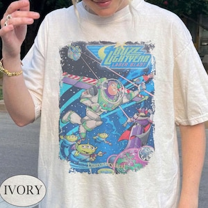 Puede incluir: Camiseta de color marfil con un gr&aacute;fico colorido de Buzz Lightyear de la pel&iacute;cula "Lightyear". El dise&ntilde;o incluye el texto "Buzz Lightyear Laser Blast" e im&aacute;genes de extraterrestres y Zurg. La camiseta tiene un aspecto vintage.
