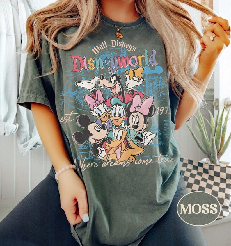 May include: Dark green t-shirt featuring a colorful graphic of Disney characters, including Mickey Mouse, Minnie Mouse, Donald Duck, and Goofy. The shirt has the text "Walt Disney's Disneyworld" and "Where dreams come true."