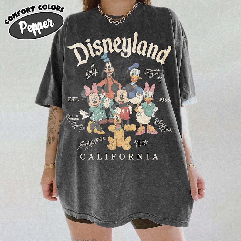 May include: Dark grey oversized t-shirt with a Disneyland graphic featuring Disney characters, the Disneyland logo, and the text "California". The shirt includes the text "EST. 1955" and the Comfort Colors Pepper logo.