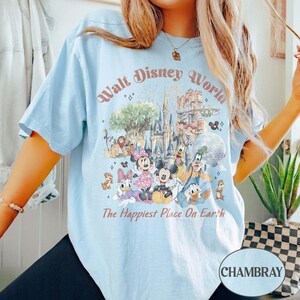 May include: Light blue t-shirt with a graphic of Disney characters and the text "Walt Disney World" and "The Happiest Place On Earth". The graphic includes Mickey Mouse, Minnie Mouse, Donald Duck, and other characters.