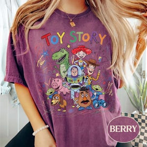 Pode incluir: Camiseta cor de berry com a inscri&ccedil;&atilde;o "TOY STORY" sobre um gr&aacute;fico colorido de personagens do filme de anima&ccedil;&atilde;o. O design inclui Woody, Buzz Lightyear e outros personagens amados. A camisa tem um visual vintage.