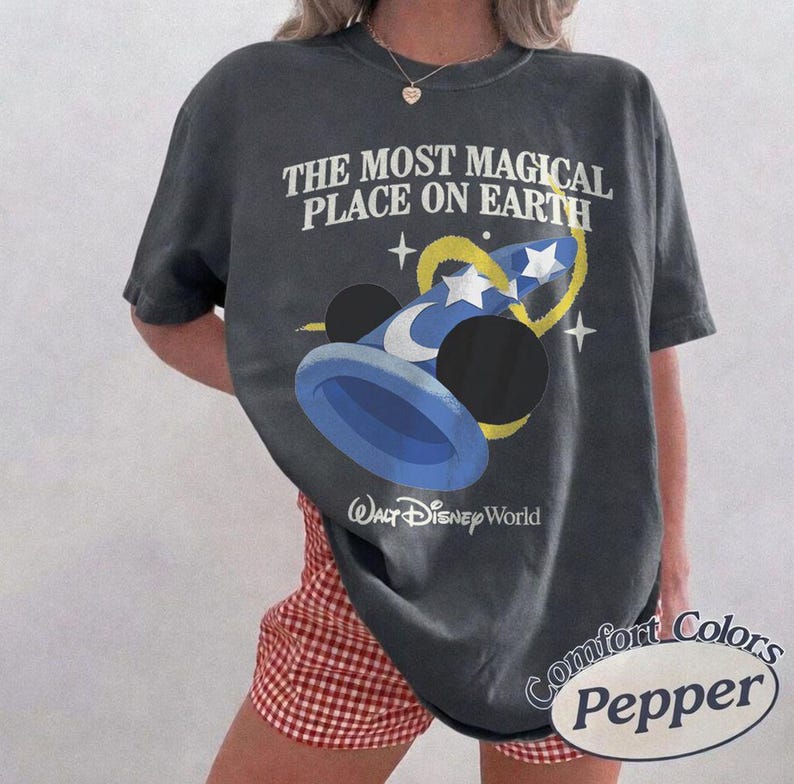 Puede incluir: Camiseta gris oscuro con el texto "THE MOST MAGICAL PLACE ON EARTH" y un gr&aacute;fico de un sombrero de mago azul con estrellas y una luna creciente. Las palabras "Walt Disney World" est&aacute;n debajo.