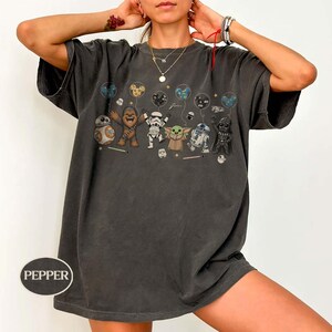 May include: Dark grey t-shirt featuring a graphic of Star Wars characters holding balloons. The characters include BB-8, Chewbacca, a Stormtrooper, Grogu, R2-D2, and Darth Vader. The word "Pepper" is printed on the bottom left of the shirt.