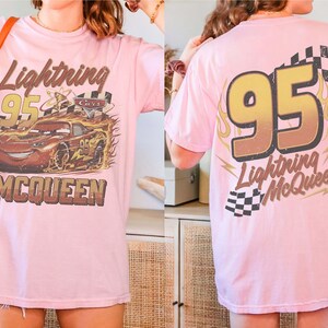 Puede incluir: Camiseta rosa claro con un gr&aacute;fico desgastado del coche de carreras Lightning McQueen, el n&uacute;mero 95 y el texto "Lightning McQueen". La parte trasera de la camiseta tambi&eacute;n muestra el n&uacute;mero 95 y el texto "Lightning McQueen".