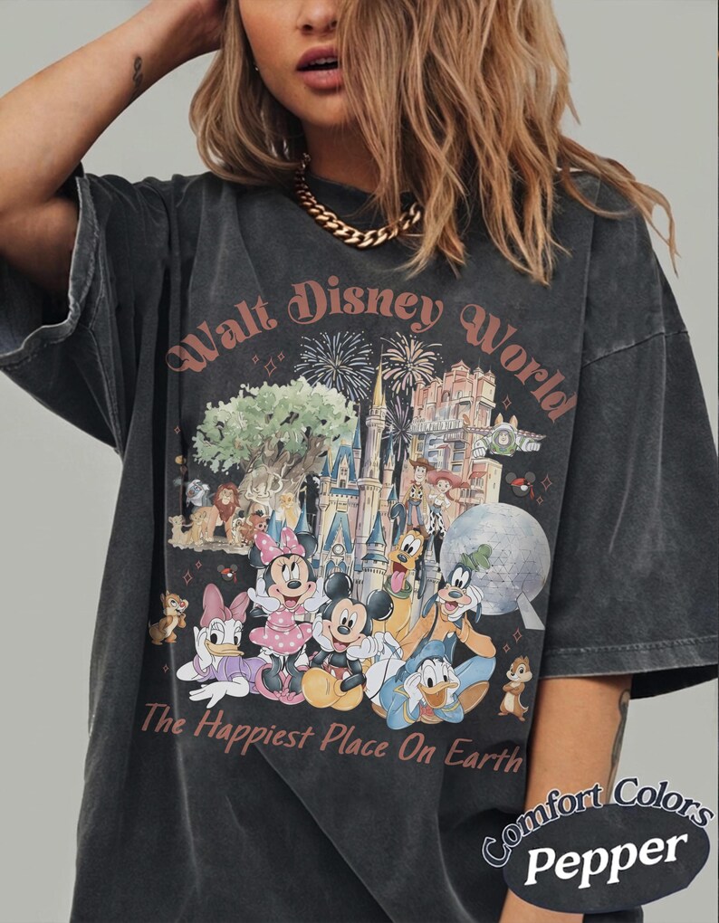 May include: Dark gray t-shirt featuring a colorful graphic of the Walt Disney World castle, characters, and fireworks. The text "Walt Disney World" and "The Happiest Place On Earth" are printed on the front. The shirt is labeled "Comfort Colors Pepper".