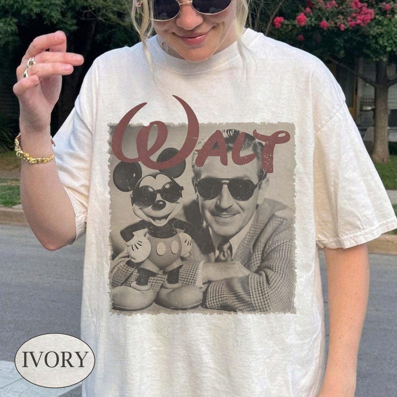 Puede incluir: Camiseta de color marfil con un gr&aacute;fico vintage de Mickey Mouse y Walt Disney con gafas de sol. La palabra "WALT" est&aacute; impresa en borgo&ntilde;a sobre la imagen. La camiseta tiene un corte cl&aacute;sico y relajado.