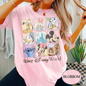 May include: A light pink t-shirt featuring a grid of Disney characters including Mickey Mouse, Donald Duck, and Stitch. The words "Walt Disney World" are printed below the characters. The word "BLOSSOM" is printed in a pink oval.