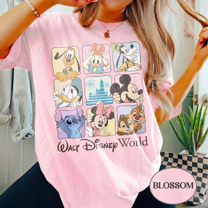 May include: A light pink t-shirt featuring a grid of Disney characters including Mickey Mouse, Donald Duck, and Stitch. The words "Walt Disney World" are printed below the characters. The word "BLOSSOM" is printed in a pink oval.