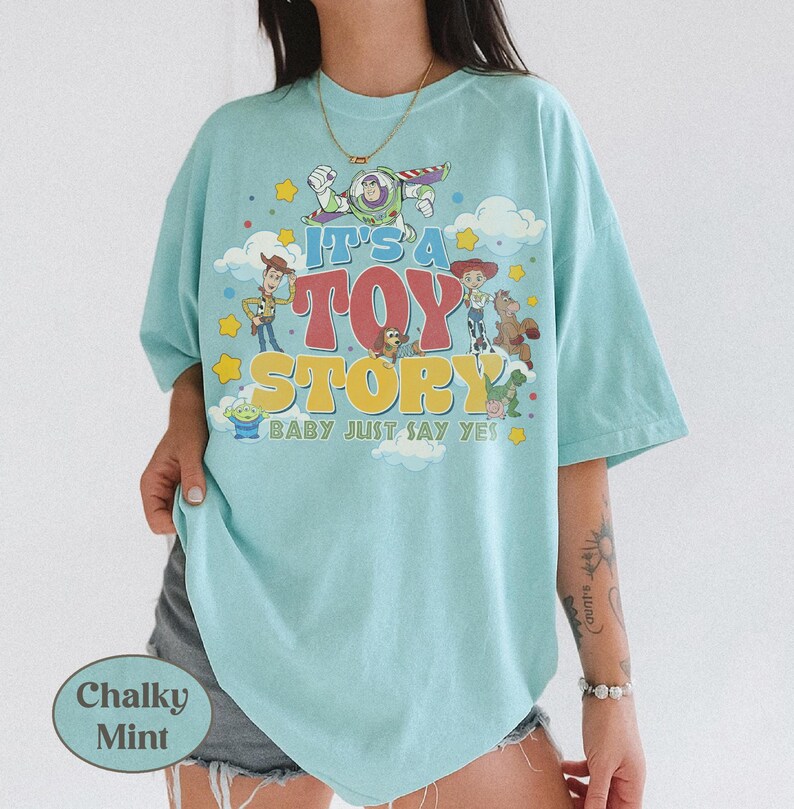 Peut inclure: Un t-shirt vert menthe clair avec une impression graphique des personnages de Toy Story, dont Woody, Buzz l'&Eacute;clair, Jessie et Zigzag. Le texte indique IT'S A TOY STORY BABY JUST SAY YES, entour&eacute; d'&eacute;toiles jaunes et de nuages blancs.