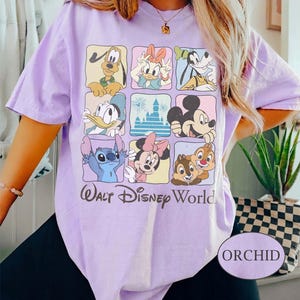 May include: Orchid-colored t-shirt featuring a grid of Disney characters including Mickey Mouse, Donald Duck, and Stitch. The words "Walt Disney World" are printed below the grid. The shirt has short sleeves.