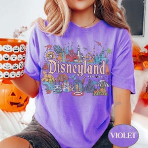 Op de afbeelding: Violetkleurig T-shirt met een Disneyland Resort-afbeelding. Het ontwerp bevat iconische parkelementen en het Disneyland-logo in vintage stijl. Een comfortabel, casual kledingstuk.