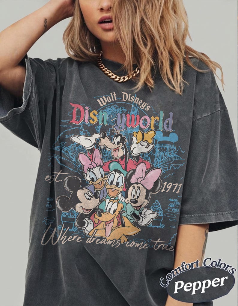 May include: Dark gray t-shirt featuring a vintage-style Walt Disney World graphic with Mickey Mouse, Minnie Mouse, Donald Duck, Daisy Duck, Goofy, and Pluto. The shirt has the text "Where dreams come true" and "est. 1971". The shirt is labeled "Comfort Colors Pepper".