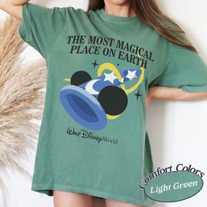Puede incluir: Camiseta verde claro con el texto "THE MOST MAGICAL PLACE ON EARTH" y un gr&aacute;fico del sombrero y las orejas de Mickey Mouse. La camiseta tambi&eacute;n tiene las palabras "Walt Disney World" impresas. La esquina inferior derecha de la camiseta dice "Comfort Colors Light Green".