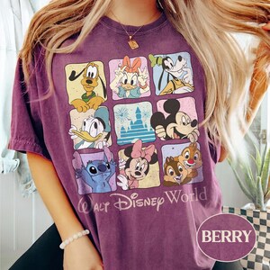 May include: Berry-colored t-shirt featuring a grid of Disney characters including Mickey Mouse, Donald Duck, and Stitch. The shirt has the words "Walt Disney World" printed below the grid. The shirt is a short-sleeved crew neck.