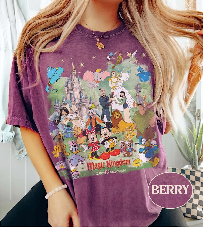 May include: Berry-colored t-shirt featuring a colorful graphic of Disney characters and the Magic Kingdom castle. The design includes Mickey Mouse, Donald Duck, and other beloved characters. The text "Magic Kingdom Walt Disney World" is printed below the characters.