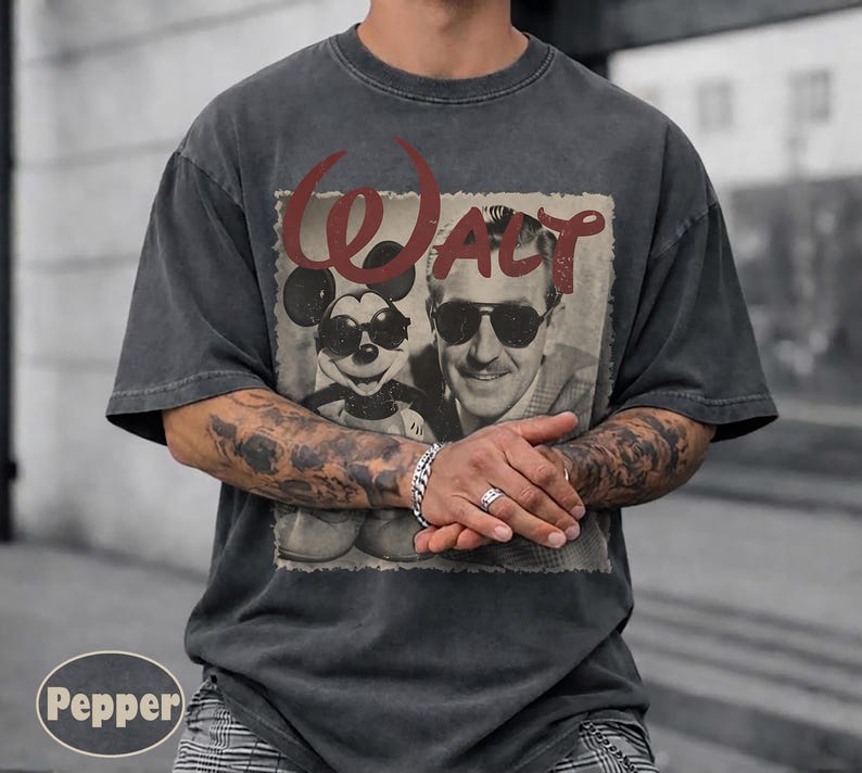 Puede incluir: Camiseta gris oscuro con un gr&aacute;fico vintage de Mickey Mouse con gafas de sol y Walt Disney. La palabra "Walt" est&aacute; en escritura roja encima de la imagen. La camiseta tiene un cuello redondo cl&aacute;sico.