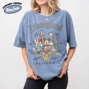 May include: Blue short-sleeved t-shirt with a Disneyland graphic. The graphic features Mickey Mouse, Minnie Mouse, Donald Duck, Goofy, Pluto, and Daisy Duck. The text "Disneyland California" is printed below the characters.