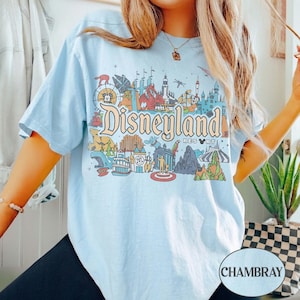 Op de afbeelding: Lichtblauw T-shirt met een kleurrijke Disneyland-afbeelding. De afbeelding bevat het Disneyland Resort-logo en diverse parkiconen. Het shirt is gemaakt van een zacht materiaal en heeft korte mouwen.