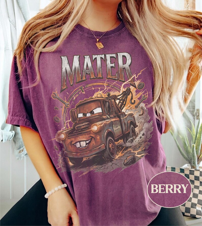 May include: A berry-colored short-sleeve t-shirt featuring a graphic print of the character Mater from the movie Cars. The design includes the text MATER in a metallic font above the brown tow truck, surrounded by wrenches and dust clouds.