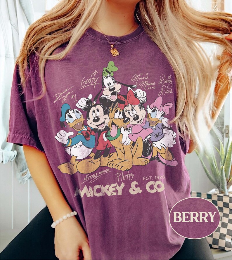K&ouml;nnte beinhalten: Beerenfarbenes T-Shirt mit einem Aufdruck von Micky Maus und seinen Freunden, darunter Donald Duck, Goofy und Pluto. Das Design enth&auml;lt Unterschriften der Charaktere und den Text "Mickey & Co. Est. 1928". Das Shirt hat einen Vintage-Look.