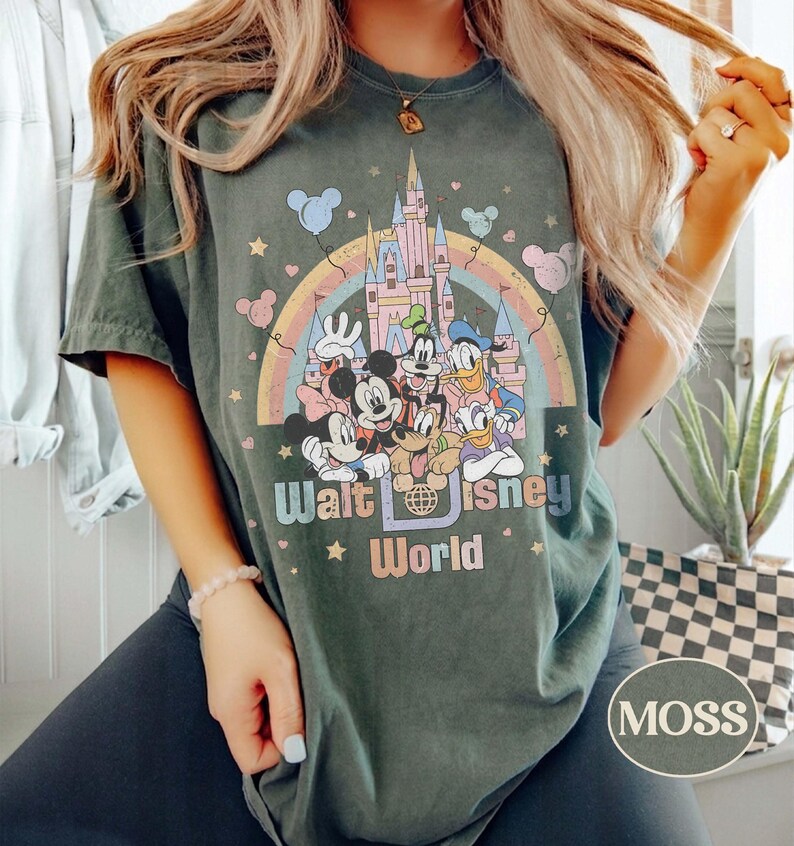 May include: Dark green t-shirt featuring a colorful graphic of Disney characters in front of a castle and rainbow. The text "Walt Disney World" is printed below the graphic. The shirt has a crew neck and short sleeves.