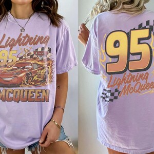 Puede incluir: Camiseta lila claro con Lightning McQueen de la pel&iacute;cula Cars. El frente muestra el coche con el texto "Lightning 95 McQueen". La parte trasera tiene un gran "95" y el texto "Lightning McQueen".