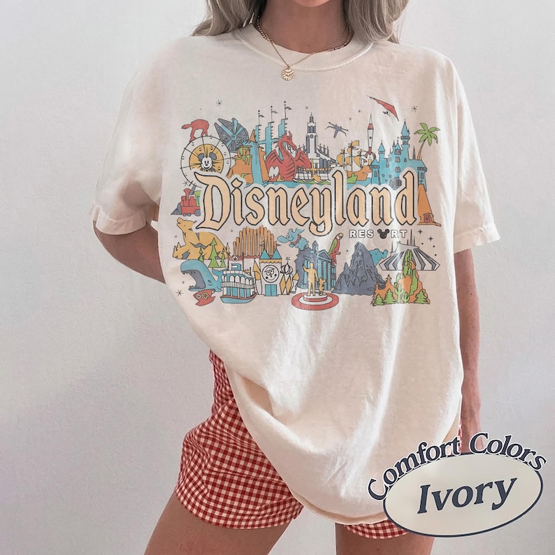 Op de afbeelding: Ivoor kleurig t-shirt met een kleurrijke Disneyland Resort afbeelding. Het ontwerp bevat iconische parkelementen en het Disneyland logo. Het shirt is van het merk Comfort Colors.