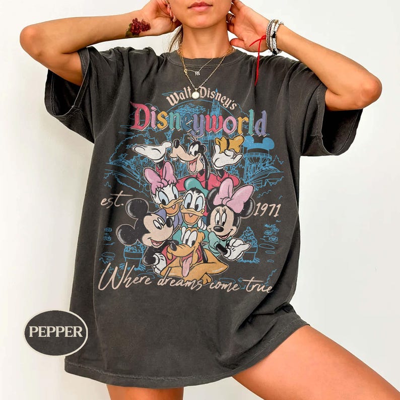 May include: Dark gray t-shirt featuring a colorful graphic of Disney characters, including Mickey Mouse, Minnie Mouse, Donald Duck, and Goofy. The shirt has the text "Walt Disney's Disneyworld" and "Where dreams come true."