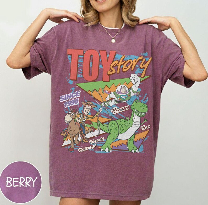 May include: Berry-colored t-shirt featuring a graphic from the movie "Toy Story." The design includes the text "Toy Story" and the characters Buzz Lightyear, Woody, Rex, and Bullseye. The shirt also has the text "Since 1995."