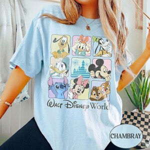 May include: Light blue t-shirt featuring a grid of Disney characters including Mickey Mouse, Donald Duck, and Stitch. The words "Walt Disney World" are printed below the grid. The shirt is made of a soft material.