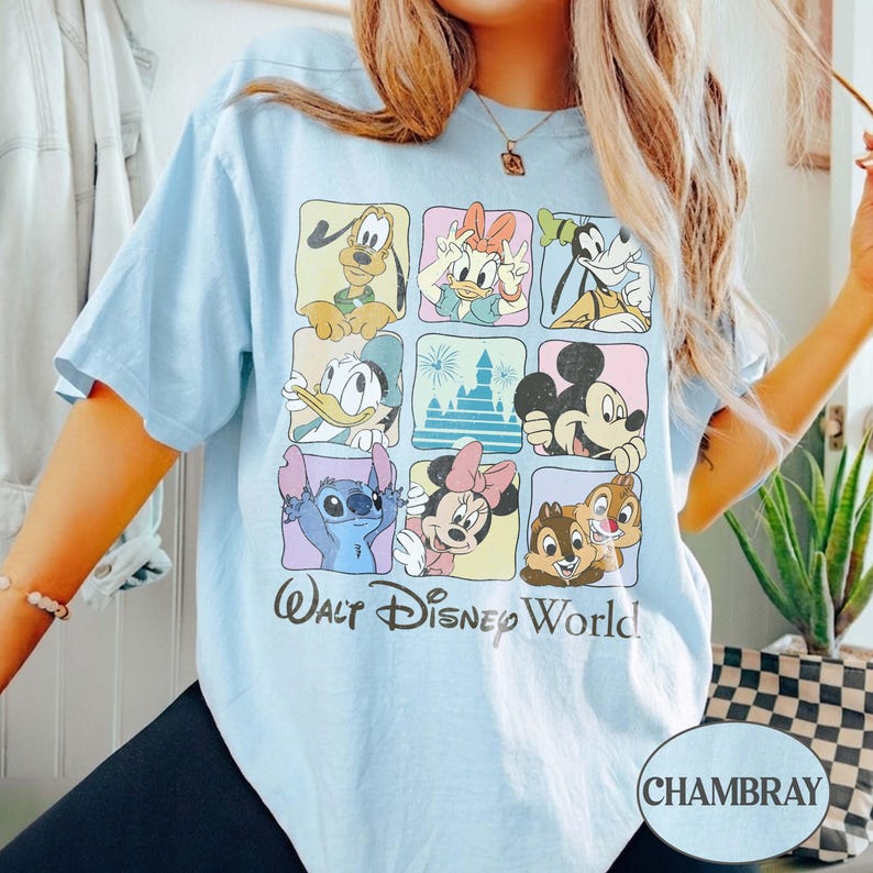 May include: Light blue t-shirt featuring a grid of Disney characters including Mickey Mouse, Donald Duck, and Stitch. The words "Walt Disney World" are printed below the grid. The shirt is made of a soft material.