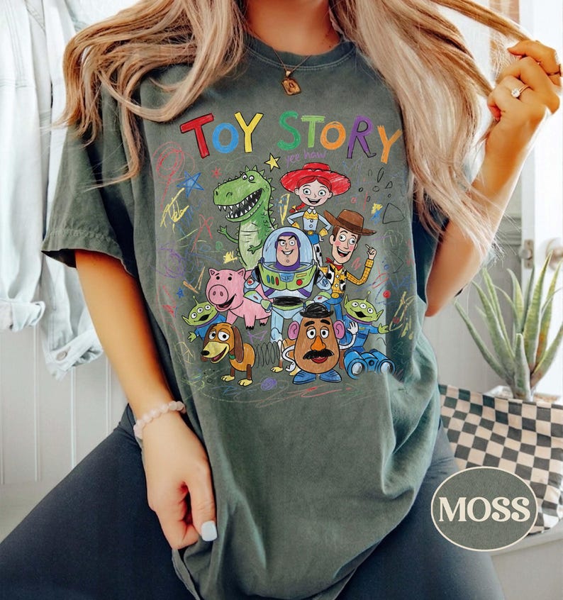 Pode incluir: Camiseta verde musgo com as palavras "TOY STORY" em letras coloridas sobre um gr&aacute;fico de personagens do filme de anima&ccedil;&atilde;o. O design inclui Woody, Buzz Lightyear, Rex e outros personagens. A camisa &eacute; de estilo casual.