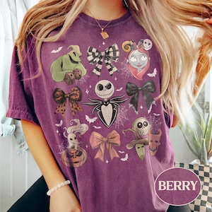 May include: A berry-colored short-sleeve t-shirt featuring a graphic print of characters and bows from The Nightmare Before Christmas, including Jack Skellington, Sally, Oogie Boogie, Zero, and the trick-or-treaters, accented with spiderwebs.