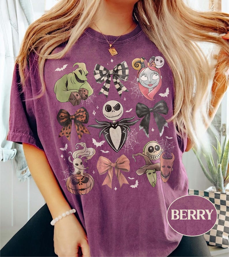 May include: A berry-colored short-sleeve t-shirt featuring a graphic print of characters and bows from The Nightmare Before Christmas, including Jack Skellington, Sally, Oogie Boogie, Zero, and the trick-or-treaters, accented with spiderwebs.