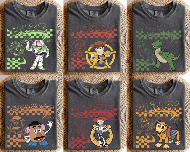 May include: Six charcoal gray t-shirts featuring Toy Story characters Buzz Lightyear, Woody, Rex, Mr. Potato Head, Jessie, and Slinky Dog. Each shirt displays the character name, a 1995 date, a checkered pattern, and a line art illustration.