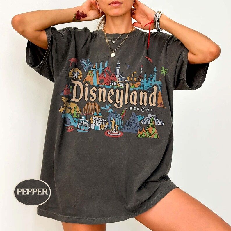 Op de afbeelding: Donkergrijs t-shirt met een kleurrijke Disneyland Resort afbeelding. Het ontwerp toont iconische bezienswaardigheden en het Disneyland Resort logo. Het shirt heeft korte mouwen en een relaxte pasvorm.