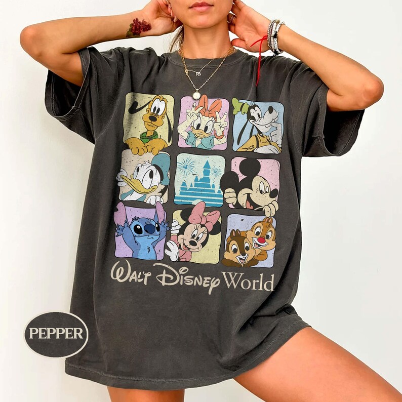 May include: Dark gray t-shirt featuring a grid of Disney characters including Mickey Mouse, Donald Duck, and Stitch. The shirt has the words "Walt Disney World" printed in a script font. The shirt is a relaxed fit.