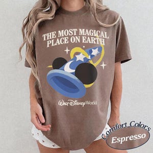 Puede incluir: Camiseta color espresso con el texto "THE MOST MAGICAL PLACE ON EARTH" y un gr&aacute;fico de un sombrero de mago azul con estrellas. El logotipo de Walt Disney World est&aacute; debajo. De la colecci&oacute;n Comfort Colors.