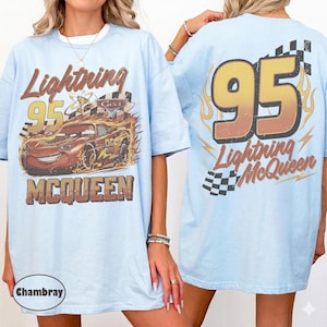 Puede incluir: Camiseta azul claro con Lightning McQueen de la pel&iacute;cula Cars. El frente muestra a McQueen con llamas y el n&uacute;mero 95. La parte posterior muestra un gran 95 con llamas y las palabras "Lightning McQueen" y una bandera a cuadros.