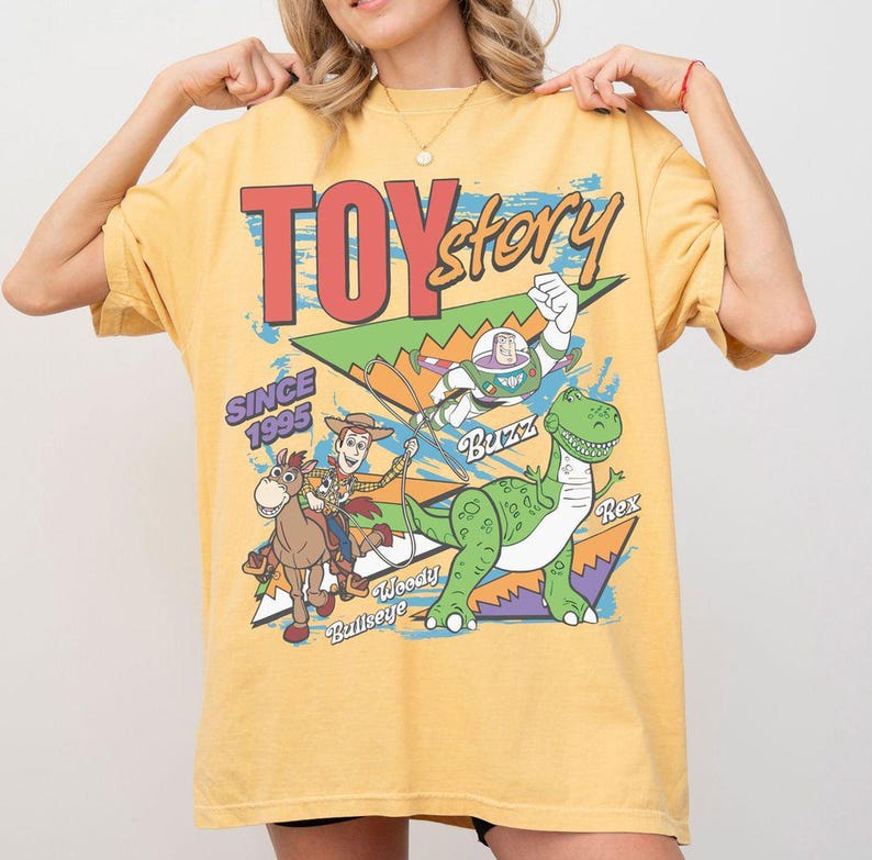 May include: Yellow t-shirt featuring a graphic from the movie Toy Story. The design includes the text "TOY STORY" in red, along with images of Woody, Buzz Lightyear, and Rex. The text "SINCE 1995" is also included.
