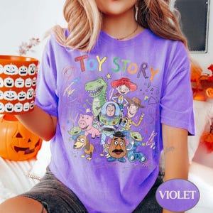 Pode incluir: Uma camiseta violeta com um gr&aacute;fico colorido de personagens do filme de anima&ccedil;&atilde;o "Toy Story". O design inclui o t&iacute;tulo do filme e v&aacute;rios personagens como Woody, Buzz Lightyear e Rex. A camisa &eacute; uma pe&ccedil;a de roupa confort&aacute;vel e casual.