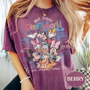 May include: Berry-colored t-shirt featuring a graphic of Disney characters including Mickey Mouse, Minnie Mouse, Donald Duck, Daisy Duck, Goofy, and Pluto. The shirt has the text "Walt Disney's Disneyworld" and "Where dreams come true" with the year "1971".