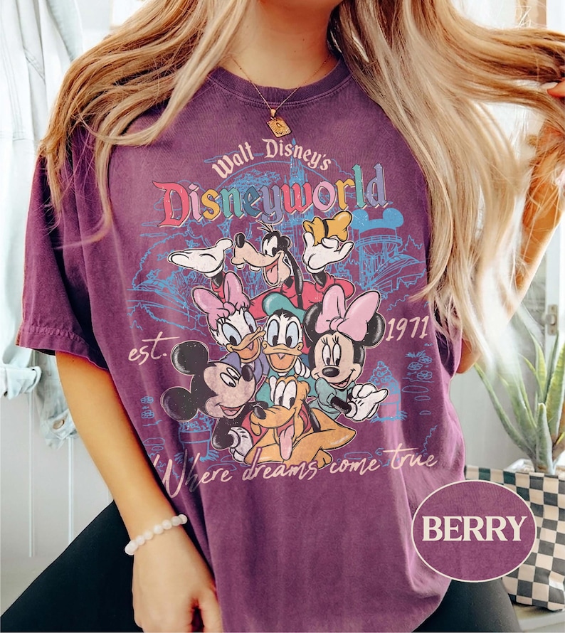 May include: Berry-colored t-shirt featuring a graphic of Disney characters including Mickey Mouse, Minnie Mouse, Donald Duck, Daisy Duck, Goofy, and Pluto. The shirt has the text "Walt Disney's Disneyworld" and "Where dreams come true" with the year "1971".